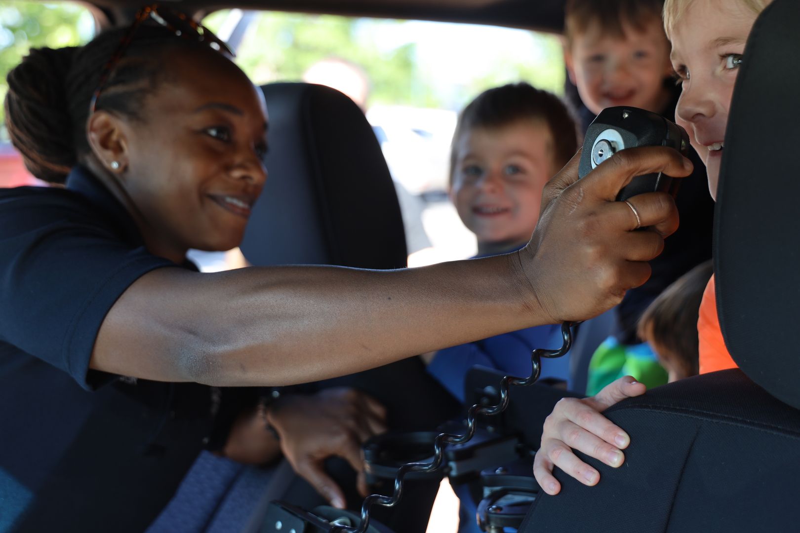 A Deputy is interacting with children and showing them how to use the radio on a patrol car.